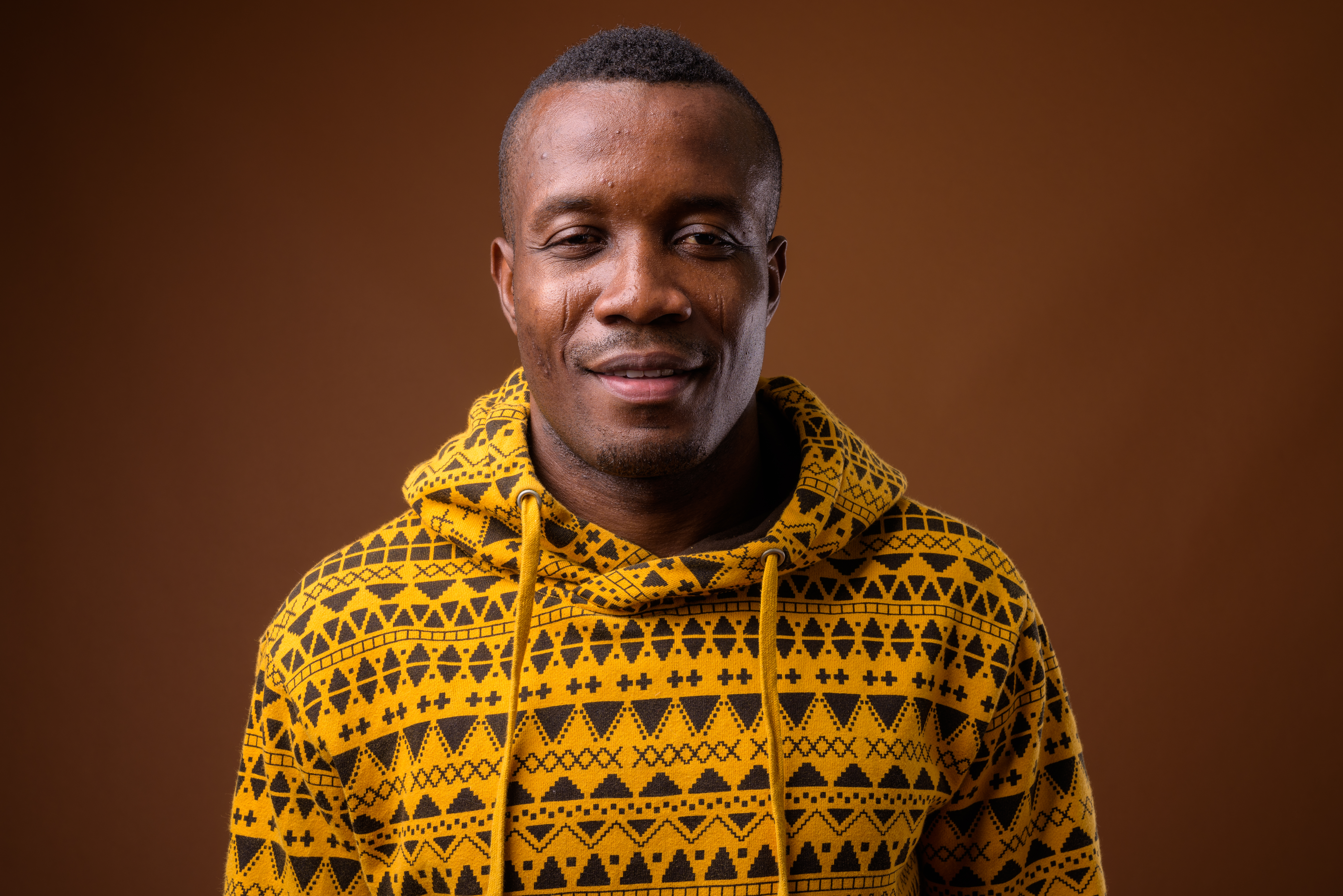 Studio shot of young African man against brown background Studio shot of young African man wearing hoodie against brown background